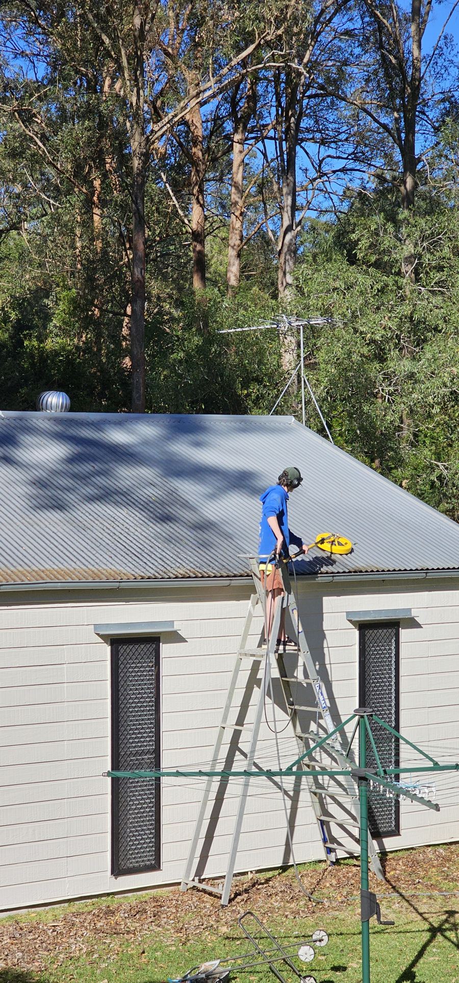 Technician on a ladder cleaning a metal roof