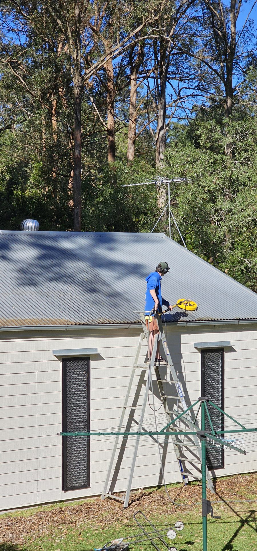 Technician on a ladder cleaning a metal roof